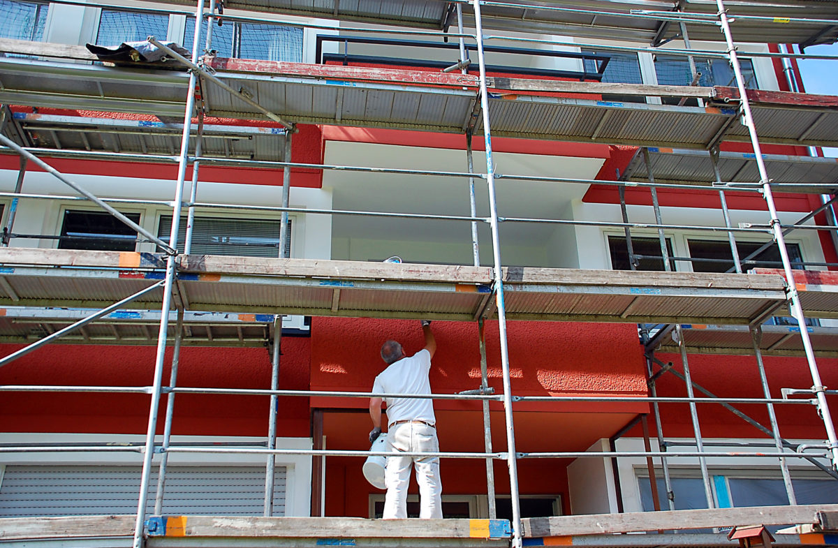 Maler steht auf einem Gerüst und streicht eine Hausfassade rot