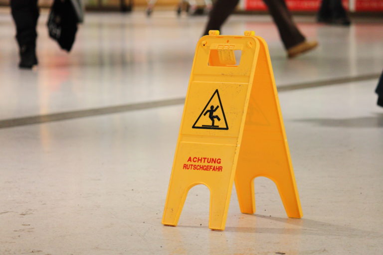 Warnschild mit Hinweis auf Rutschgefahr auf einem Gehweg