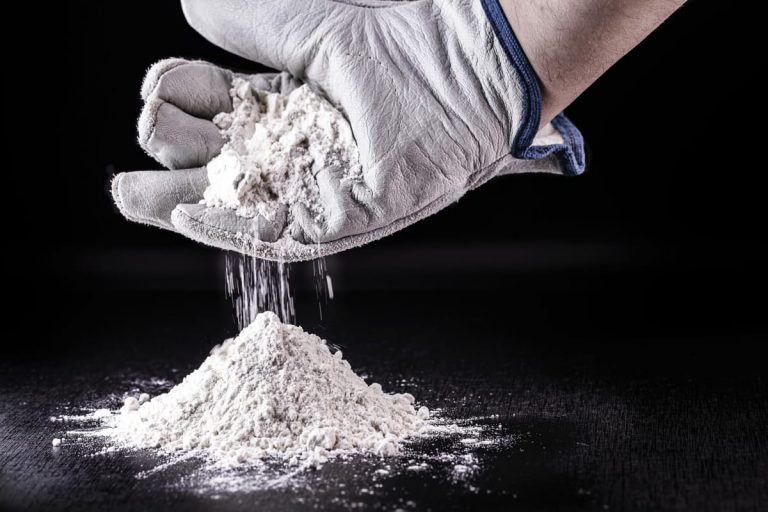 Titandioxid rieselt von einer Hand mit Handschuh auf den Boden. Schwarzer Hintergrund.