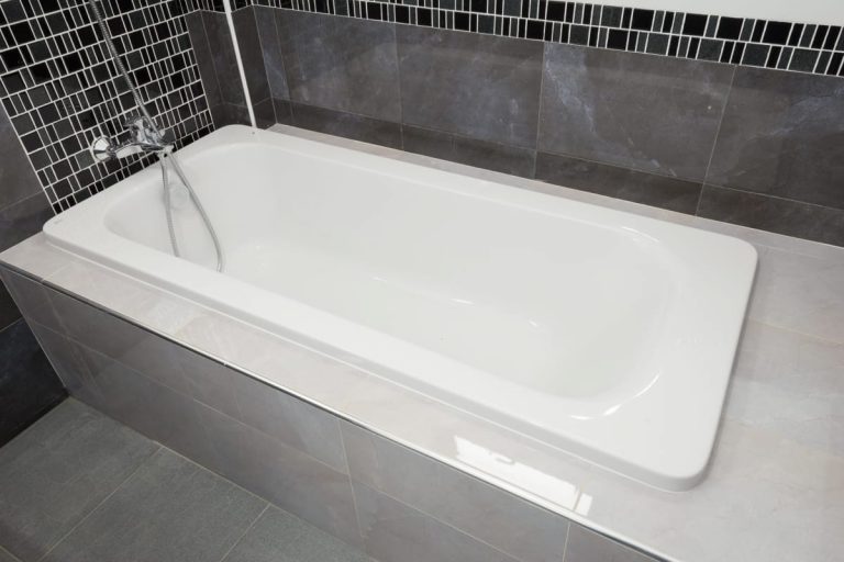 Moderne weiße Badewanne umgeben von großen hell- und dunkelgrauen Fliesen