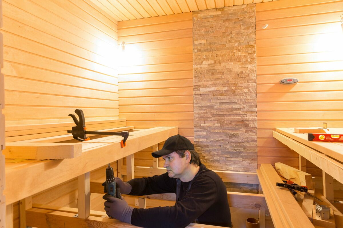 Handwerker schraubt ein Holzbauteil in einer Sauna fest