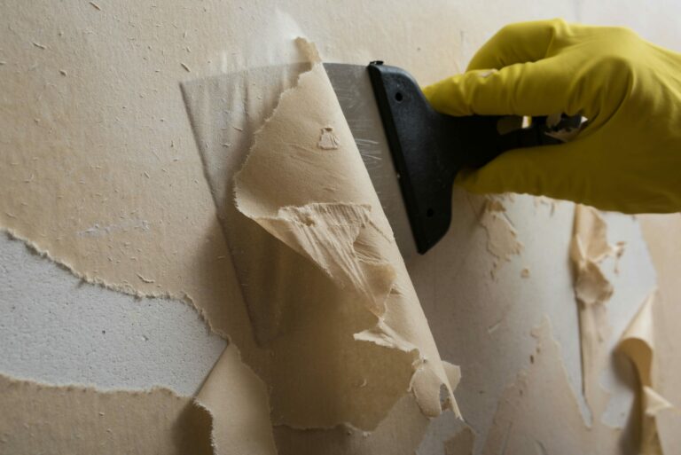 Handwerker entfernt alte und vergilbte Tapete von einer weißen Wand