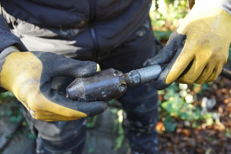 Handwerker hält eine Rohrreinigungsdüse aus Metall. Er trägt gelbe Handschuhe
