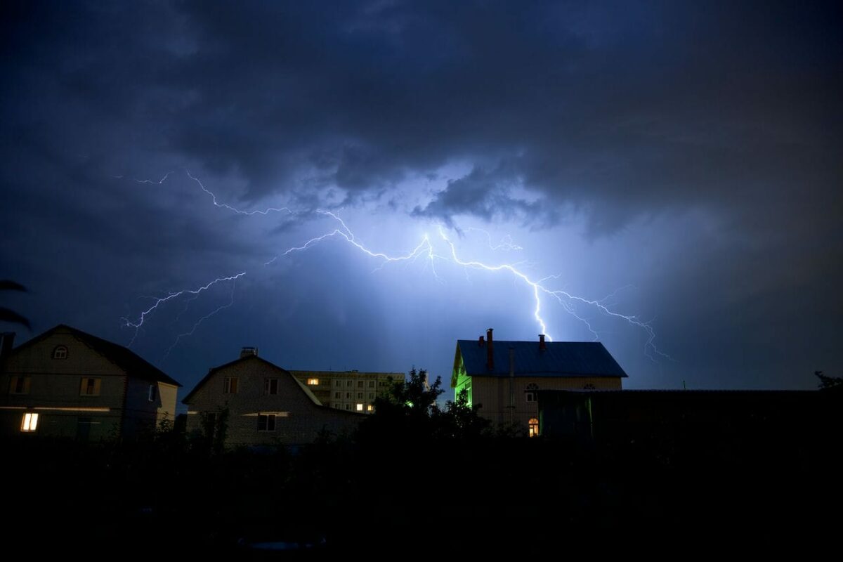 Blitz schlägt in einem Wohngebiet ein. Es ist dunkel, nur der Blitz erhellt das Foto.