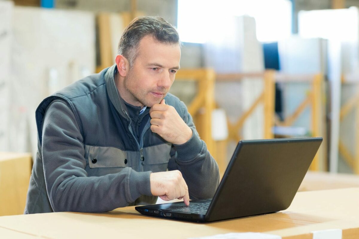 Handwerker sitzt in der Werkstatt vor einem Laptop und wirkt nachdenklich
