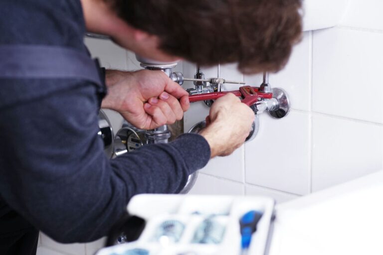 Sanitärinstallateur baut ein Waschbecken ein und schraubt an einem Siphon