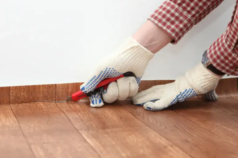Bodenleger trägt Handschuhe und schneidet Linoleum an einer Wand zu
