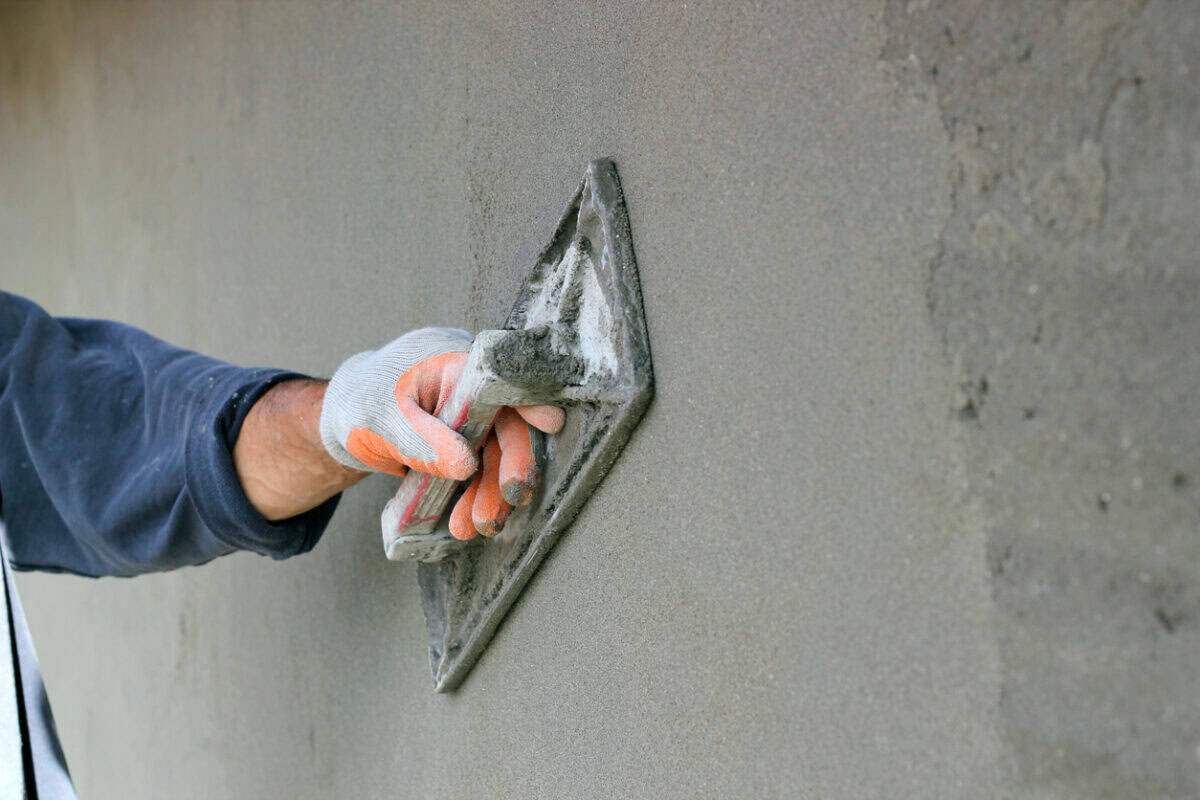 Ein Handwerker verputzt eine Wand mit dunkelgrauem Putz