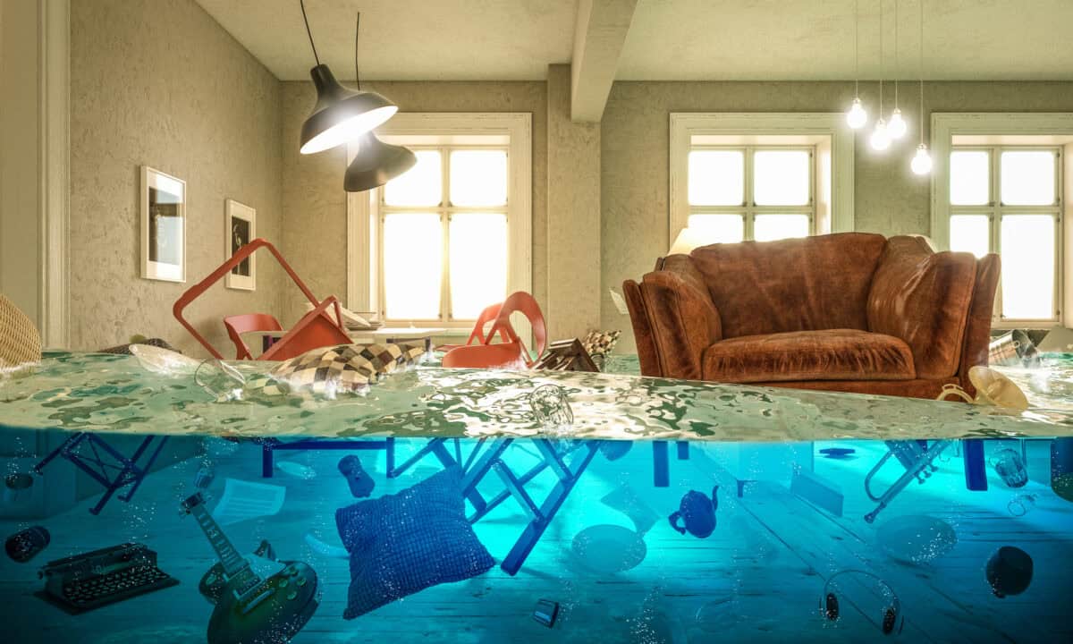 Ein überschwemmtes Zimmer mit schwimmenden Objekten: Ein Sessel, eine Schreibmaschine, Wohnaccessoires und Stühlen.