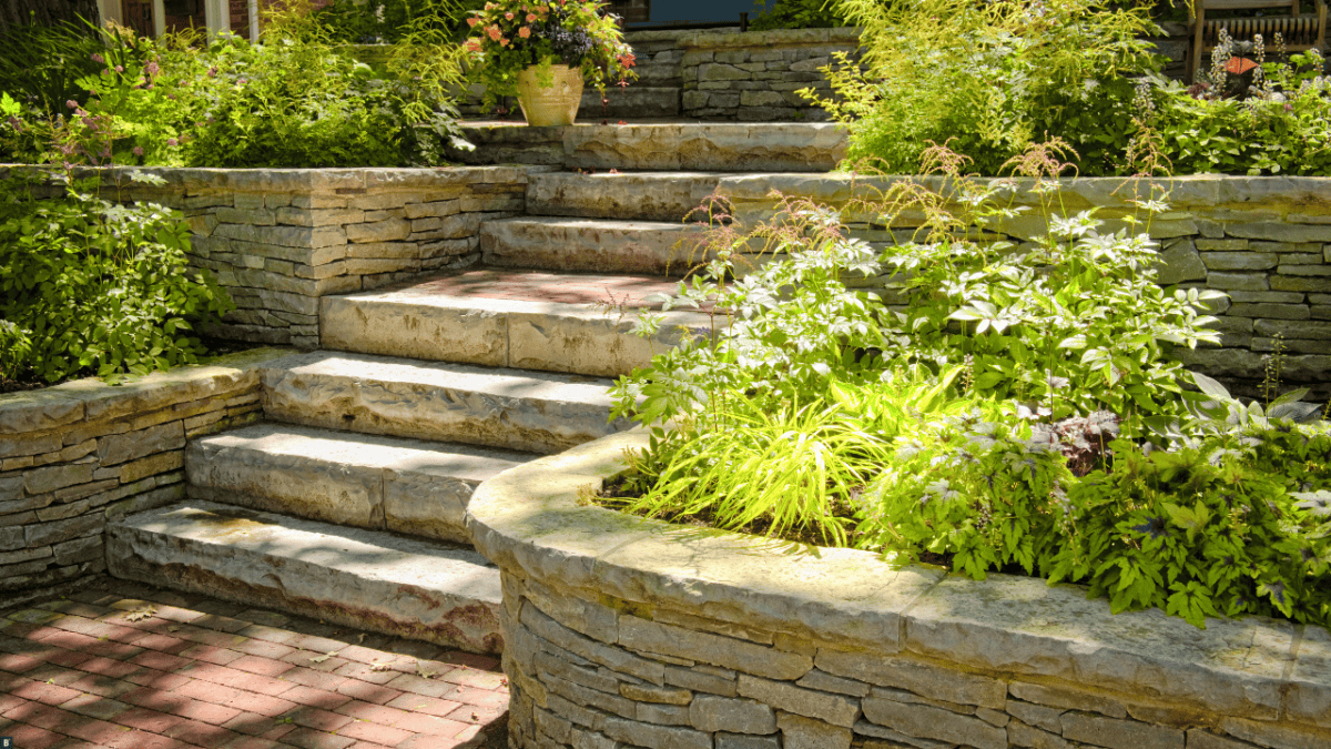 Ein Garten mit seitlichen Beeten in verschiedenen Höhen und einer Treppe in der Mitte, alles mit Naturstein.
