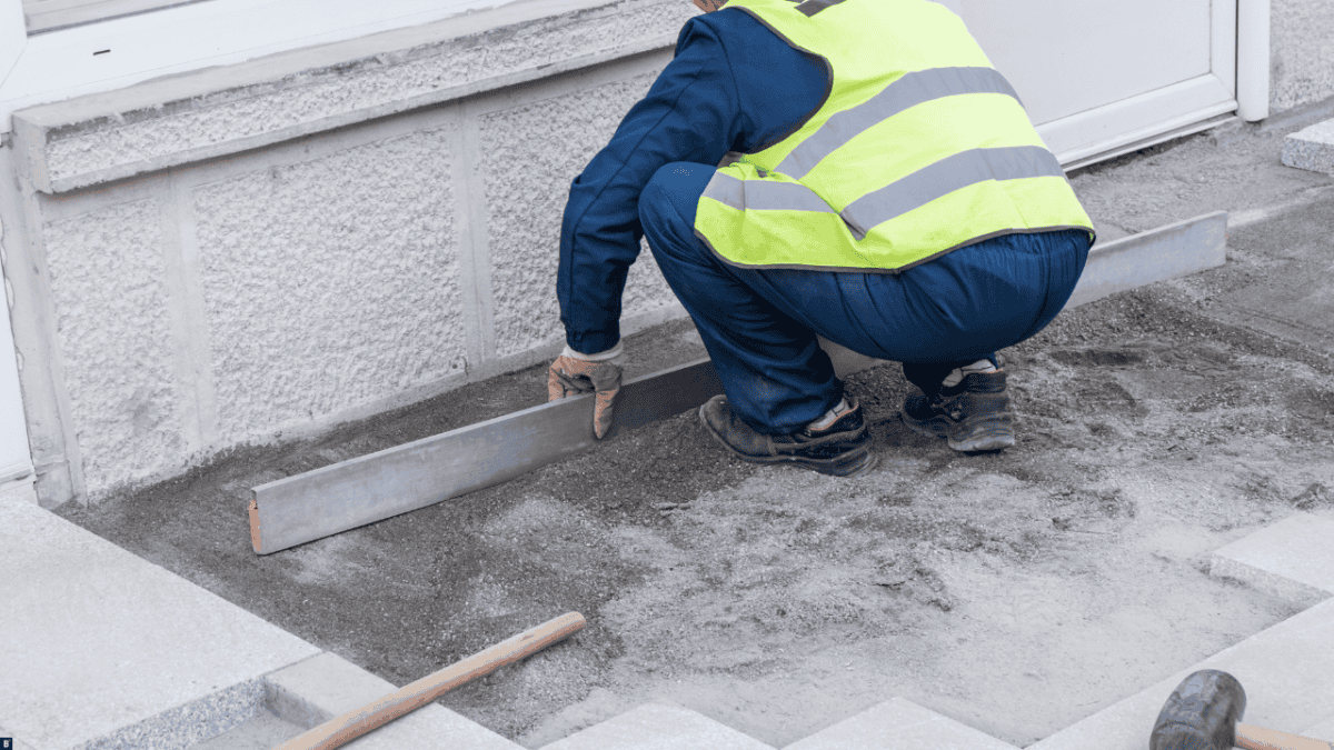 Ein Mann begradigt den Schotter, um Terrassenplatten zu verlegen.