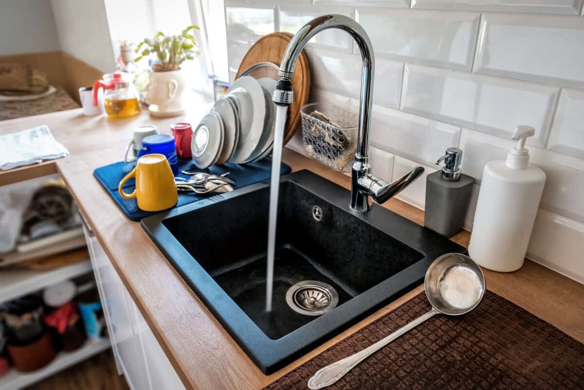 Es läuft vom Wasserhahn aus Wasser in die schwarze Küchenspüle