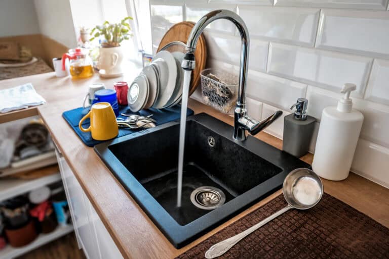 Es läuft vom Wasserhahn aus Wasser in die schwarze Küchenspüle